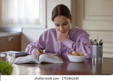 Serious Teen Girl School Pupil Studying Alone Sitting At Kitchen Table. Focused Teenage Student Reading Book, Making Notes Doing Homework At Home. Adolescent Tween Distance Learning Education Concept