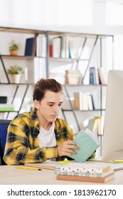 Serious Teenage Boy In Black And Yellow Shirt Sitting At Desk At Home And Reading Students Books For Upcoming Classes