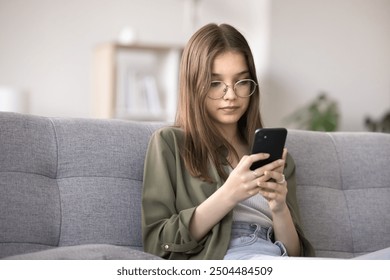 Serious teenager girl using cellphone at home, watching videos on streaming movies and TV platforms, playing mobile games, chatting with friends through messenger. Modern gadgets overuse, bad habit - Powered by Shutterstock