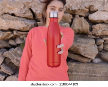 Serious Teenager In Pink Hoodie With Red Water Bottle In Hand Looking Stright. Short-haired Teen Girl Staying Outdoors Near Stone Wall. Clothing And Reusable Water Bottle Mockup