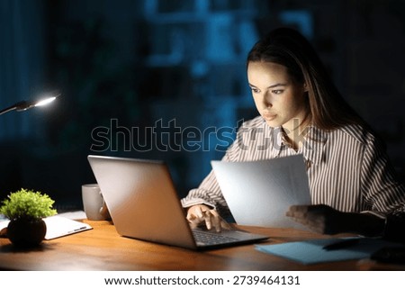Serious teleworker working in the night checking document and using laptop at homeoffice