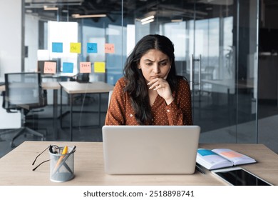 Serious thinking businesswoman at work with laptop inside office, female office worker prepares electronic report presentation on computer, thoughtfully studies financial and investment indicators. - Powered by Shutterstock