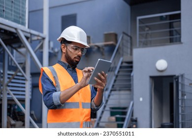 Serious thinking and focused engineer working in factory in hard hat and vest, man using tablet computer reading diagram, and checking equipment, inside industrial factory. - Powered by Shutterstock