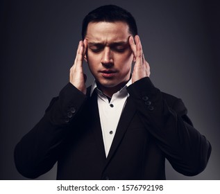 Serious thinking man with thought-transference abilities holding the hands the head with closed eyes in black suit on grey studio background. Closeup portrait. 