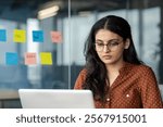 Serious thinking woman working with laptop inside office close up. Focused businesswoman reading from laptop screen working in casual clothes and glasses at workplace.