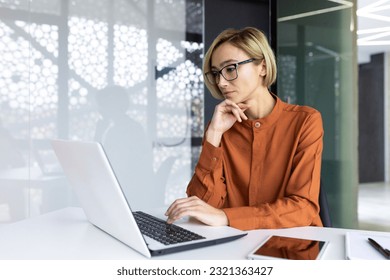 Serious thinking woman working with laptop inside office at workplace, businesswoman solving technical task, female programmer coding new software. - Powered by Shutterstock