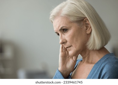Serious thoughtful blonde elderly woman worried about health problems, thinking over retirement, touching dry facial skin, face, looking away, feeling depressed. Side casual portrait - Powered by Shutterstock