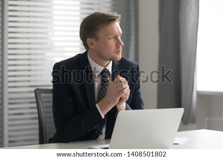 Serious thoughtful businessman wear suit sit at office desk with laptop feel doubtful concerned about business challenge, pensive anxious ceo looking away thinking solving work problem at workplace