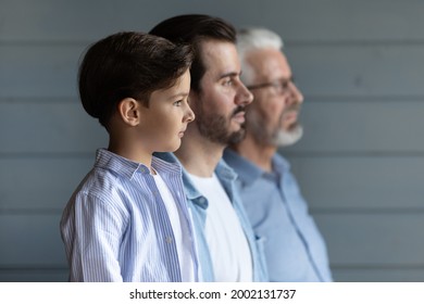 Serious Thoughtful Cute Boy Kid Standing In Row With Young Father And Senior Grandfather, Looking Forward, Thinking Of Future. Intergenerational Family Portrait With Three Male Generations