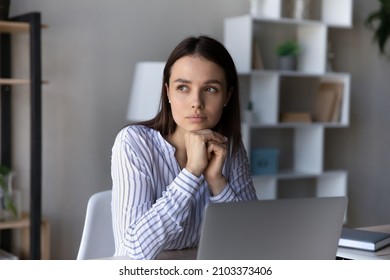 Serious thoughtful employee sitting at table with laptop, looking at window away, thinking over business problems, project, future career vision, feeling doubts, uncertain, dreaming and pondering - Shutterstock ID 2103373406
