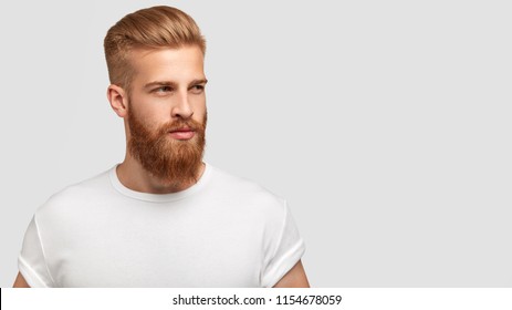 Serious thoughtful male with ginger beard, dressed casually, focused somewhere, isolated over white background with free space on right for your advertising content. Pensive red haired hipster