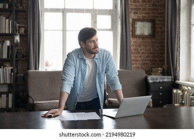 Serious thoughtful millennial business man standing at laptop and documents, leaning on work table in home office loft interior, looking away, thinking over creative ideas for project, making - Powered by Shutterstock