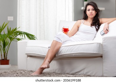 Serious thoughtful woman staring intently at the camera as she sits relaxing on a sofa with her mobile and a cocktail in a low angle view