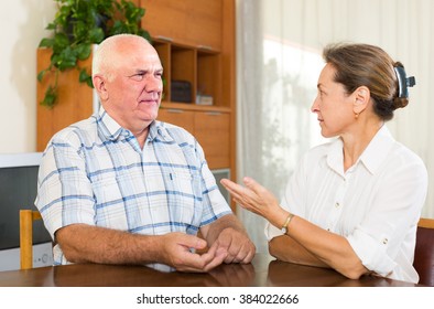 Serious Unhappy Mature Couple Talking In Home Interior. Focus On Man