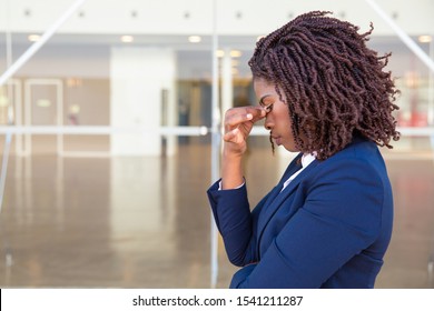 Serious Upset Female Employee Thinking Over Bad News Outside Office. Young African American Business Woman Standing At Glass Wall With Head Low, Touching Face, Looking Into Vacancy. Bad News Concept