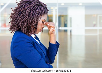 Serious Upset Female Employee Thinking Over Bad News Outside Office. Young African American Business Woman Standing At Glass Wall With Head Low, Touching Face, Looking Into Vacancy. Bad News Concept