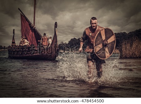 Serious viking warrior in the attack, running along the shore with Drakkar on the background.