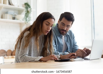 Serious wife and husband planning budget, checking finances, focused young woman using calculator, counting bills or taxes, man using laptop, online banking services, sitting at table in kitchen - Powered by Shutterstock