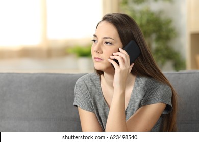 Serious Woman Attending A Phone Call Sitting On A Sofa In The Living Room At Home