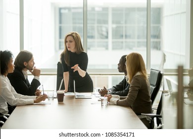 Serious woman boss scolding employees for bad results or discussing important instructions at multiracial team meeting, dissatisfied female executive talking to multiracial team at boardroom briefing