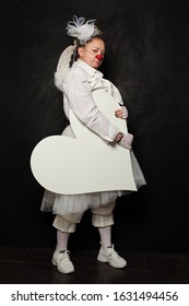 Serious Woman In Clown Costume Holding White Empty Heart Banner On Black Background