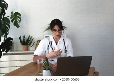 Serious Woman Doctor Talking To Patient On Laptop Video Call From The Hospital Office. Female Health Care Worker Telling Bad News To The People Of Deceased Family Member Over Webcam From The Clinic.