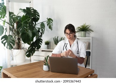 Serious Woman Doctor Talking To Patient On Laptop Video Call From The Hospital Office. Female Health Care Worker Telling Bad News To The People Of Deceased Family Member Over Webcam From The Clinic.