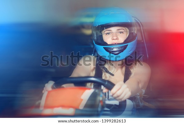 serious woman in helmet driving car for\
karting with other people in sport club\
indoor