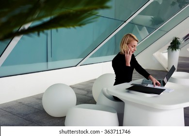 Serious woman lawyer analyzing court case on paper documents and net-book while calling with mobile phone to client, female economist talking on cell telephone while sitting with laptop before meeting