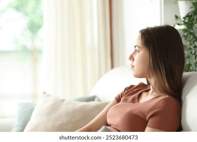 Serious woman looking through a window sitting on a sofa at home - Powered by Shutterstock