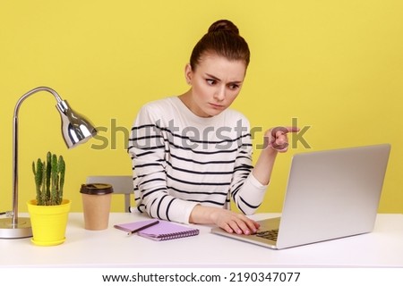 Serious woman office employee sitting on workplace, scolding, saying I have told you, looking laptop display while having video call. Indoor studio studio shot isolated on yellow background.