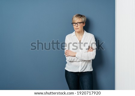 Serious woman standing with folded arms over a blue background looking intently at the camera with a stern implacable expression with copyspace