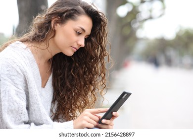 Serious woman using cell phone sitting on a bench in the street