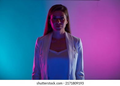 Serious Woman In White Business Suit Low Light Portrait With Neon Lights Colors Effect. Female Model Isolated On Neon Background