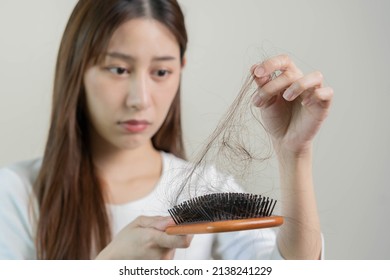 Serious, worried asian young woman, girl holding brush, show her comb, hairbrush with long loss hair problem after brushing, hair fall out on her hand in living room. Health care, beauty treatment. - Shutterstock ID 2138241229