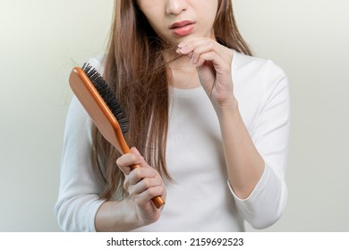 Serious, worried asian young woman, girl holding brush, show her comb, hairbrush with long loss hair problem after brushing, hair fall out on her hand in living room. Health care, beauty treatment. - Shutterstock ID 2159692523