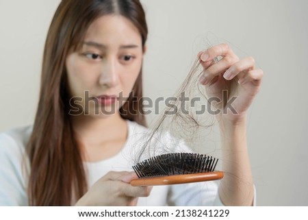Serious, worried asian young woman, girl holding brush, show her comb, hairbrush with long loss hair problem after brushing, hair fall out on her hand in living room. Health care, beauty treatment.