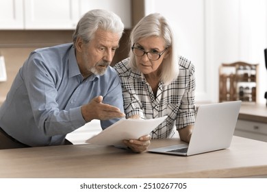 Serious worried older couple read legal documents letter, checking domestic bills stand at kitchen table with laptop, feel disappointed due to subpoena, high taxes, overdue, bad news, money shortage - Powered by Shutterstock