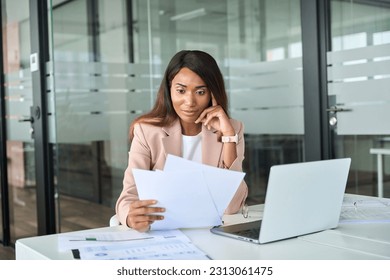 Serious young African American business woman account manager executive expert checking tax documents, analyzing financial bills reading corporate marketing papers working sitting at office desk. - Shutterstock ID 2313061475