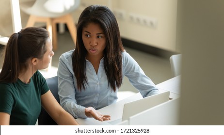 Serious Young African American Businesswoman Talking With Female Coach In Boardroom At Meeting. Confident Mixed Race Manager Presenting New Business Concept With Woman Colleague Discuss.