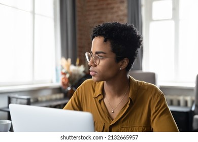 Serious Young African Business Woman Wearing Eyeglasses, Sitting At Office Workplace With Laptop, Looking Away With Pensive Face, Thinking Of Project Future Vision, Problem Solving, Planning Tasks