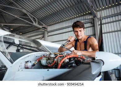 Serious Young Aircraft Mechanic Standing And Fixing Small Airplane