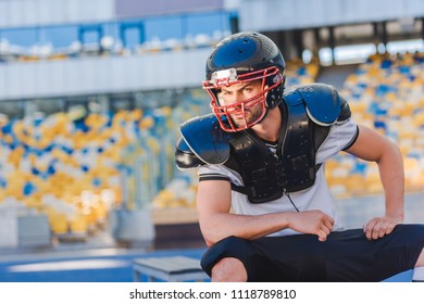 serious young american football player sitting at sports stadium - Powered by Shutterstock