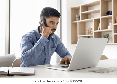 Serious young Arab business man talking on cellphone, work app, client online service on laptop, Internet technology for job telephone conversation, typing, giving consultation - Powered by Shutterstock