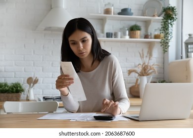 Serious young Asian woman, renter, homeowner checking, calculating utility bill, seeing mistaken too high costs, looking at paper receipt with doubt, having problems with mortgage, taxes fee payment