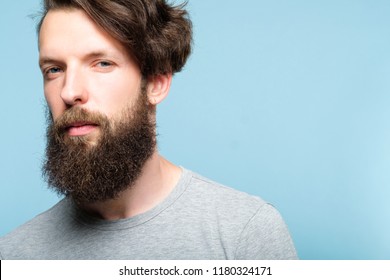 Serious Young Bearded Guy With Penetrating Look. Confident Business Trainer Or Life Coach. Casual Hipster With Stylish Hairdo. Portrait Of A Handsome Man On Blue Background.