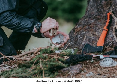 Serious young bearded hiker in cap setting fire in the forest using a flint rock. Various methods of starting a campfire. Survival skills. - Shutterstock ID 2046931907