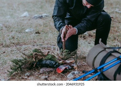 Serious young bearded hiker in cap setting fire in the forest using a wood sticks. Various methods of starting a campfire. Survival skills. - Shutterstock ID 2046931925