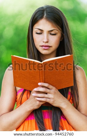 serious young, beautiful girl holding an open book, read background summer green park