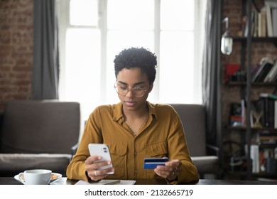 Serious young Black bank customer woman paying for purchase, domestic fees, bills by blue plastic credit card, using online payment app on smartphone, shopping on internet stores - Powered by Shutterstock